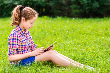 diz dijital tablet ile çimlerde oturan, okuma ve sörf, açık portre rahat güzel genç kız giyimi