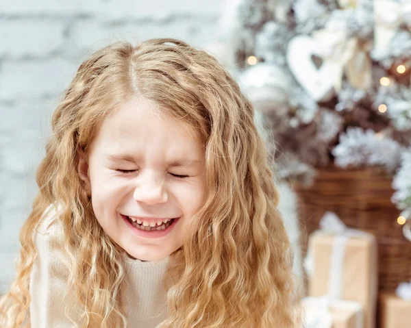 Roztomilá blonďatá holčička se zavřenýma očima, sedí pod vánoční stromeček a směje se, detailní portrét — Stock fotografie