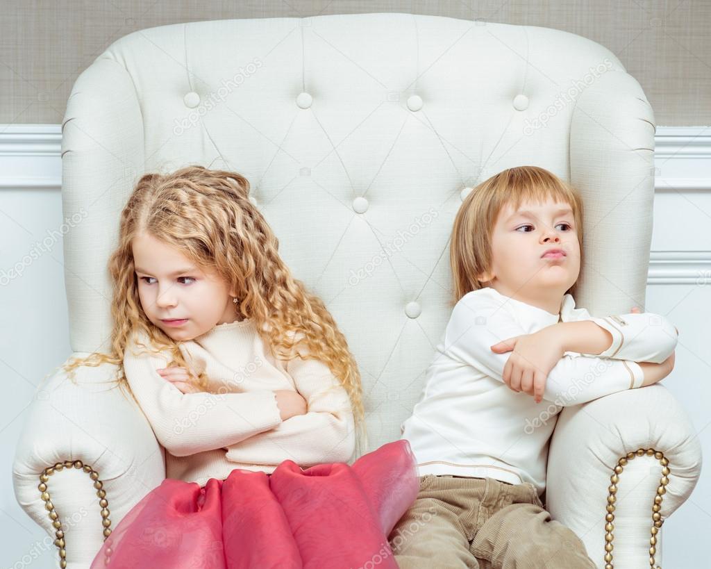 Cute little siblings (boy and girl) being at odds with each other, sitting on armchair