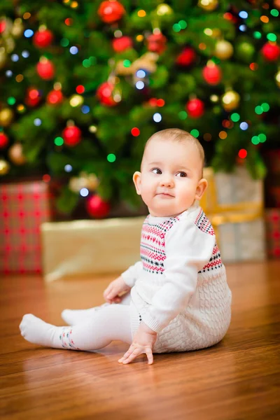Cute little baby girl sitting in front of Christmas tree with colorful lights and a lot of gift boxes Stock Image