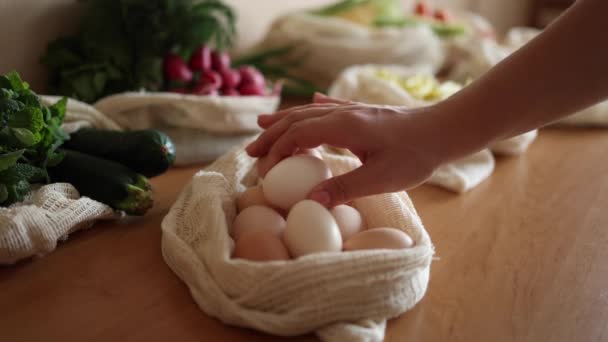 Γυναικείο χέρι πάρει αυγό από τσάντα παντοπωλείου καμβά. Λαχανικά σε επαναχρησιμοποιήσιμα οικολογικά βαμβακερά σακουλάκια σε ξύλινο τραπέζι. Καμία ιδέα για ψώνια αποβλήτων. Πλαστικά είδη — Αρχείο Βίντεο