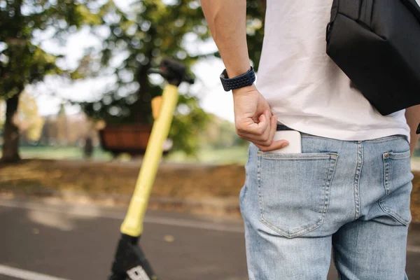 Vista posterior del hombre con bolso de hombro negro tomar su teléfono desde el bolsillo trasero para conectar un e-scooter — Foto de Stock