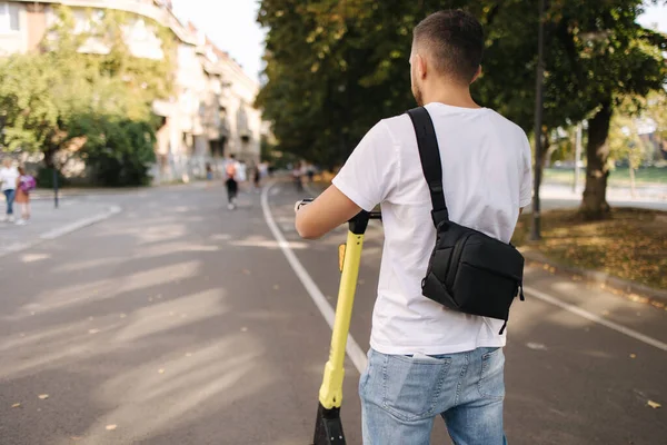 Mladík jezdí na elektrickém skútru na schůzce. Ekologický dopravní koncept. Fešák venku s e-skútrem. Zadní pohled — Stock fotografie