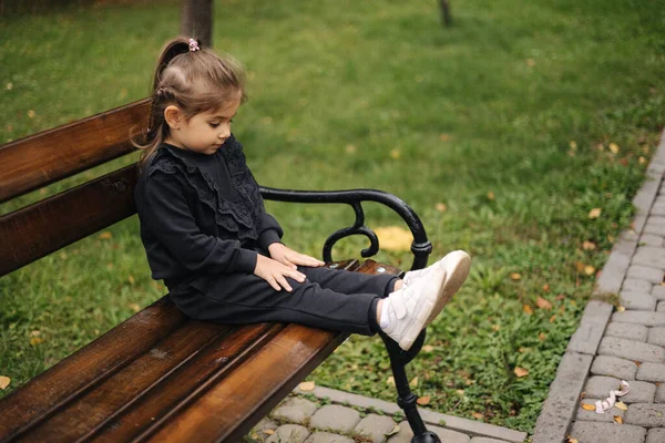 Cute little girl in beautiful black suit sitting on the bench. Autumn mood — Stock Photo, Image