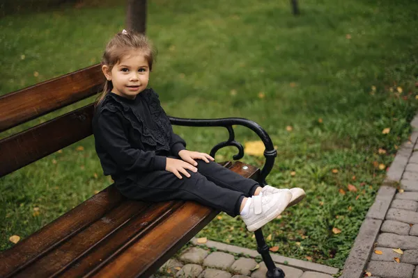 Menina bonito em belo terno preto sentado no banco. Humor de outono — Fotografia de Stock