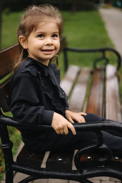 Retrato de linda niña en traje negro hermoso sentado en el banco. Humor de otoño — Foto de Stock