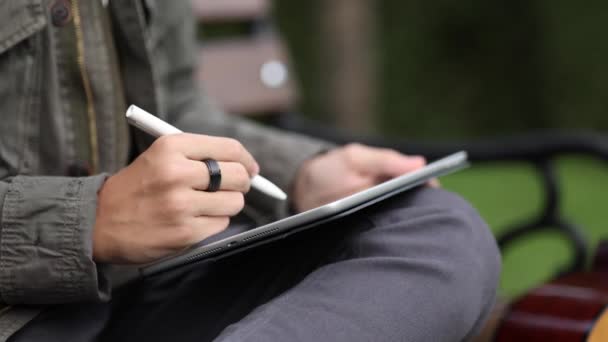 Крупним планом хлопчик малює в планшеті за допомогою олівця. Молодий дизайнер використовує планшет на відкритому повітрі. осінній час — стокове відео