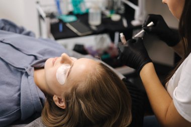 Güzellik stüdyosunda kirpik yapan bir kadın. Sarı saç modelinin kirpikleri için boyası, kıvırcığı, kaplaması ve uzantısı var.