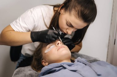 Genç manken için kirpik kaplama prosedürleri yapan bir güzellik uzmanı. Modern kirpik bakım prosedürleri laminasyon ve kirpiklerin genişletilmesi. Profesyonel güzellik salonu..