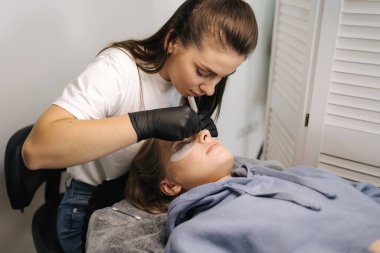 Genç manken için kirpik kaplama prosedürleri yapan bir güzellik uzmanı. Modern kirpik bakım prosedürleri laminasyon ve kirpiklerin genişletilmesi. Profesyonel güzellik salonu..