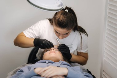 Genç manken için kirpik kaplama prosedürleri yapan bir güzellik uzmanı. Modern kirpik bakım prosedürleri laminasyon ve kirpiklerin genişletilmesi. Profesyonel güzellik salonu..