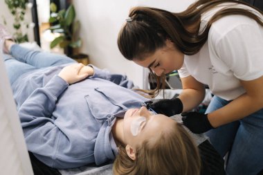 Genç manken için kirpik kaplama prosedürleri yapan bir güzellik uzmanı. Modern kirpik bakım prosedürleri laminasyon ve kirpiklerin genişletilmesi. Profesyonel güzellik salonu..