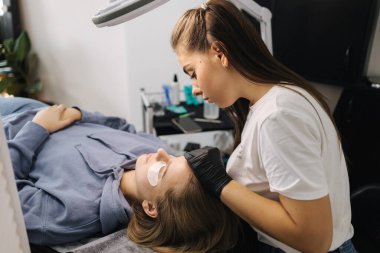 Genç manken için kirpik kaplama prosedürleri yapan bir güzellik uzmanı. Modern kirpik bakım prosedürleri laminasyon ve kirpiklerin genişletilmesi. Profesyonel güzellik salonu..