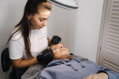 Güzellik stüdyosunda kirpik yapan bir kadın. Sarı saç modelinin kirpikleri için boyası, kıvırcığı, kaplaması ve uzantısı var. Siyah eldivenler