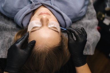 Güzellik stüdyosunda kirpik yapan bir kadın. Sarı saç modelinin kirpikleri için boyası, kıvırcığı, kaplaması ve uzantısı var. Birinci kişi görünümü