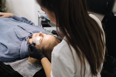 Güzellik stüdyosunda kirpik yapan bir kadın. Sarı saç modelinin kirpikleri için boyası, kıvırcığı, kaplaması ve uzantısı var. Siyah eldivenler