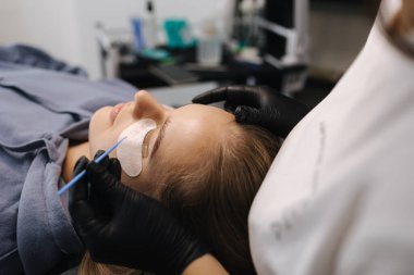 Güzellik stüdyosunda kirpik yapan bir kadın. Sarı saç modelinin kirpikleri için boyası, kıvırcığı, kaplaması ve uzantısı var. Siyah eldivenler