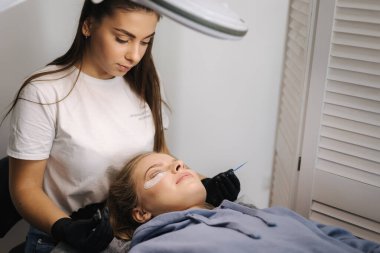 Genç manken için kirpik kaplama prosedürleri yapan bir güzellik uzmanı. Modern kirpik bakım prosedürleri laminasyon ve kirpiklerin genişletilmesi. Profesyonel güzellik salonu..
