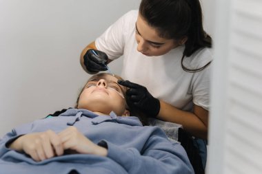 Genç manken için kirpik kaplama prosedürleri yapan bir güzellik uzmanı. Modern kirpik bakım prosedürleri laminasyon ve kirpiklerin genişletilmesi. Profesyonel güzellik salonu.