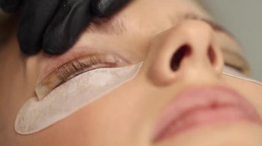 Kirpik tedavisi prosedürlerine yakın çekim. Güzel bir kadın, sarı saç modeli kirpikleri var. Kadın kirpikleri boyuyor, kıvırıyor, kaplıyor ve uzatıyor. Makro video