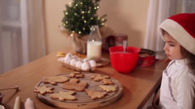 Noel Baba şapkalı küçük kız evde zencefilli ekmek süslüyor. Noel ve Yeni Yıl gelenekleri. Noel pastanesi. Mutlu tatiller.