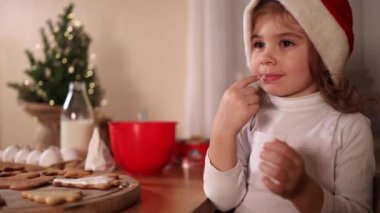 Noel Baba şapkalı küçük kız evde zencefilli ekmek süslüyor. Noel ve Yeni Yıl gelenekleri. Noel pastanesi. Mutlu tatiller.