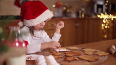 Noel Baba şapkalı küçük kız evde zencefilli ekmek süslüyor. Noel ve Yeni Yıl gelenekleri. Noel havası