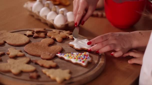 Mão da mãe ajuda filha decora pão de gengibre usando esmalte branco. Conceito de tradições de Natal e Ano Novo. Humor de Natal — Vídeo de Stock