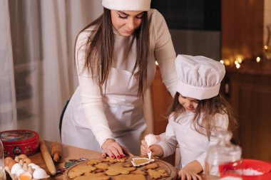 Noel Baba şapkalı anne küçük kızıyla zencefilli ekmeği jöleli süsledi. Noel ve Yeni Yıl gelenekleri. Noel pastanesi. İyi tatiller.
