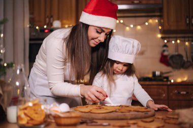 Noel Baba şapkalı anne küçük kızıyla zencefilli ekmeği jöleli süsledi. Noel ve Yeni Yıl gelenekleri. Noel pastanesi. İyi tatiller.