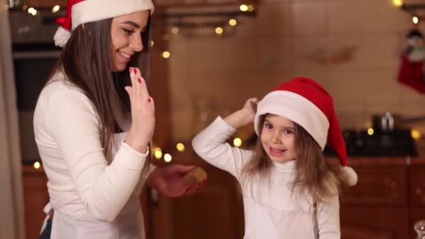 Two girls in santa hat spent time very happy at the kitchen. Christmas holidays — Stock Video
