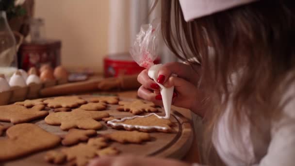 Gadis kecil bertopi santa menghiasi roti jahe menggunakan glasir putih. Konsep tradisi Natal dan Tahun Baru. Toko roti Natal. Selamat berlibur — Stok Video