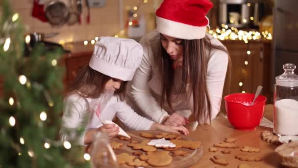 Мама в капелюсі в Сантасі зі своїм маленьким пончиком прикрашає імбирні пряники вдома. Різдвяна і новорічна традиції. Різдвяна пекарня. Щасливих свят — стокове відео