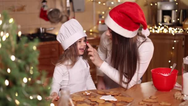 Mom in santas hat with her little doughter decorates gingerbread at home. Christmas and New Year traditions concept. Christmas bakery. Happy holidays — Stock Video