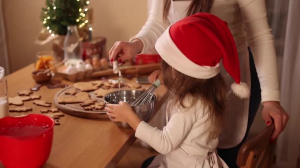 Glückliche kleine Mädchen mit ihrer schönen Mutter machen Lebkuchen zu Hause. Weihnachtsdekoration in der Küche. Tanne mit Lichterketten — Stockvideo