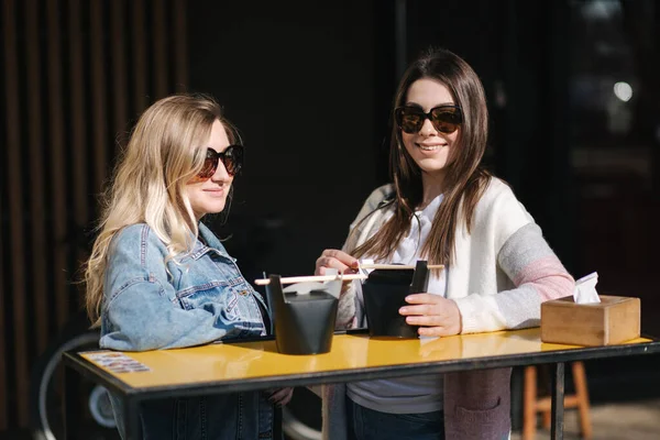 Dos hermosas chicas rubias y morenas piden comida china para llevar. Habla la joven al aire libre. Primavera día soleado —  Fotos de Stock