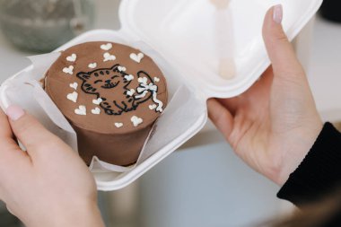 Kadın kedi ve beyaz şeker kalplerle dolu bento kekini ahşap kaşık ile çevreci paketinde tutuyor.
