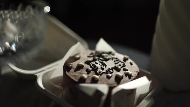 Шоколадный пирог в экологической коробке с деревянной ложкой. Белые свечи и бокалы для шампанского на роскошном мраморном столе — стоковое видео