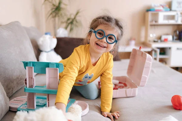 Adorable little girl smile and playing doctor in her room. Cute three year old girl spend time playing. Girls wearing glasses yellow blouse and blue leggings. Ukrainian cute kid — стоковое фото