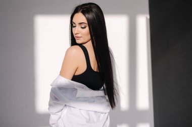 Beyaz duvarın önünde duran mavi kotlu ve beyaz gömlekli güzel esmer kadın. Beyaz arkaplanda gölge