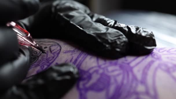 Primer plano del maestro del tatuaje haciendo tatuaje negro con pintura. Master trabaja con guantes negros estériles. Joven artista del tatuaje en el trabajo. Máquina de tatuaje inalámbrica — Vídeos de Stock