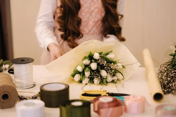 Una mujer hace un ramo de primavera. Floristería femenina envolviendo hermoso ramo de flores de primavera en papel de paquete sobre la mesa. Hermosa composición floral —  Fotos de Stock