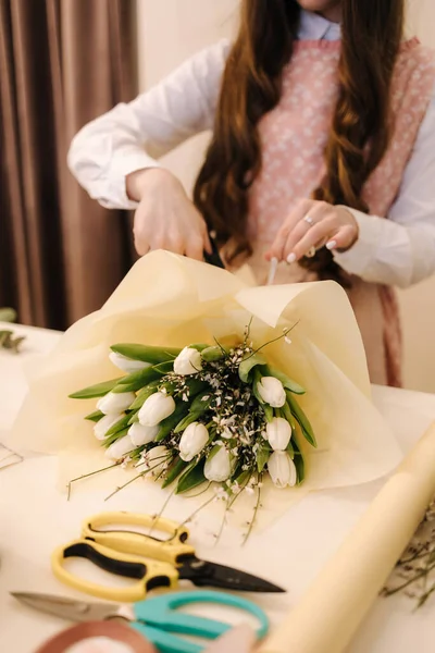 Woman make spring bouquet. Female florist wrapping beautiful bouquet of spring flowers in pack paper on the table. Beautiful flower composition —  Fotos de Stock