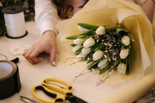 Una mujer hace un ramo de primavera. Floristería femenina envolviendo hermoso ramo de flores de primavera en papel de paquete sobre la mesa. Hermosa composición floral —  Fotos de Stock