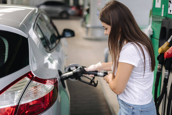 Attractive young woman refueling car at gas station. Female filling diesel at gasoline fuel in car using a fuel nozzle. Petrol concept. Side view. Fuel shortage in Ukraine