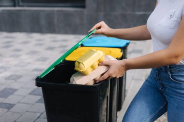 Dişi seçiliminde iki çöp, plastik şişe ve yumurta kutusu bulunur ve farklı geri dönüşüm kutularına konur. Kadına yakın çekim: Mavi, yeşil ve yeşil çöp tenekesi.