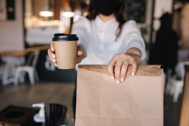 Bir kadın tek kullanımlık kahve ve yiyecek dolu bir paket bulundurur. Taka away konsepti. Mesaj için yer. Orta santral. Yakın çekim.