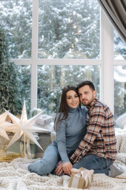 Genç ve güzel bir çift kadın ve erkek büyük bir rüzgarın önünde oturuyor, dışarıda kar var. Noel zamanı mutlu bir aile.