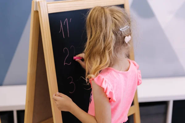 Little girl writes numbers on a board. Kindergarten.