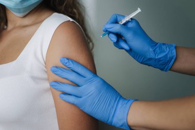 Koruyucu eldivenli kadın doktor elinde şırıngayla kovid 19 aşısı yapıyor. Omuzlarına iğne batırılan kadınlar. Aşı klinik deney konsepti, korona virüsü..